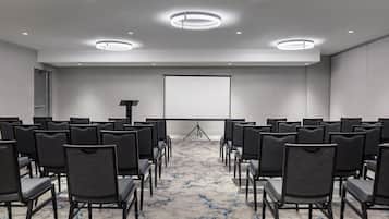 A conference room with rows of chairs facing a projection screen, a podium, and a carpeted floor.