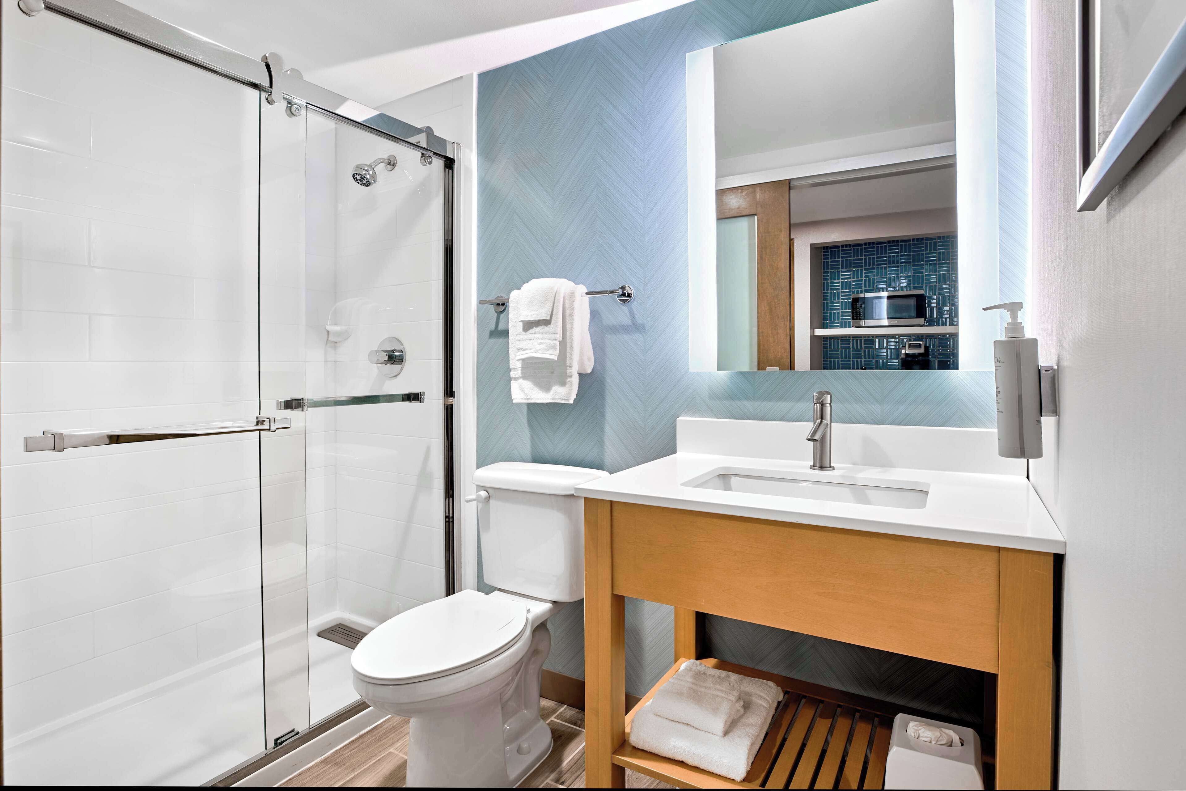 A modern bathroom with a glass shower enclosure, a white toilet, a sink with a wooden vanity, and a mirror above the sink.