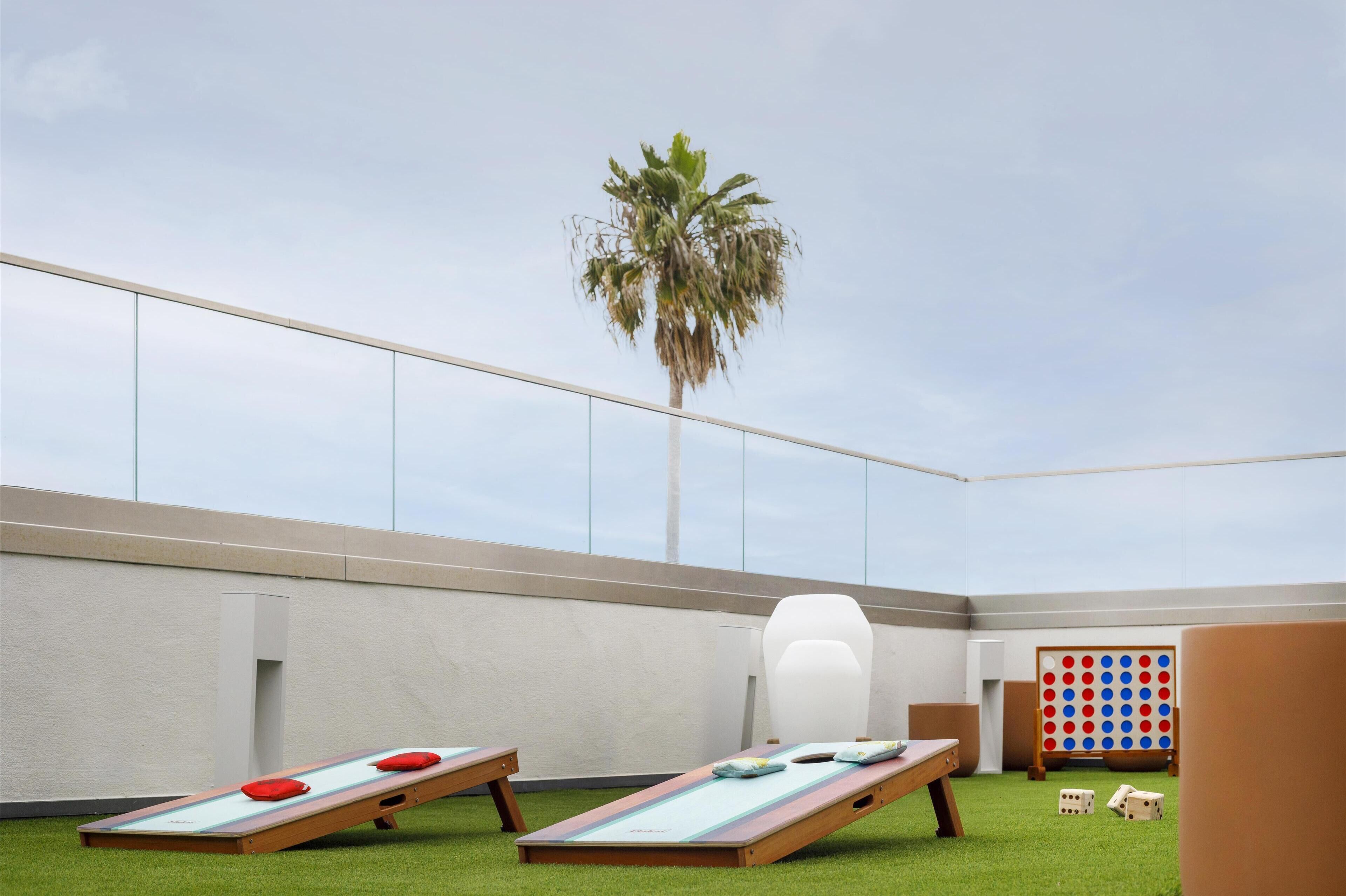 A rooftop lounge with two sun loungers, a palm tree, and a board game area.