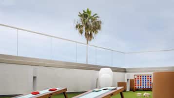 A rooftop lounge with two sun loungers, a palm tree, and a board game area.