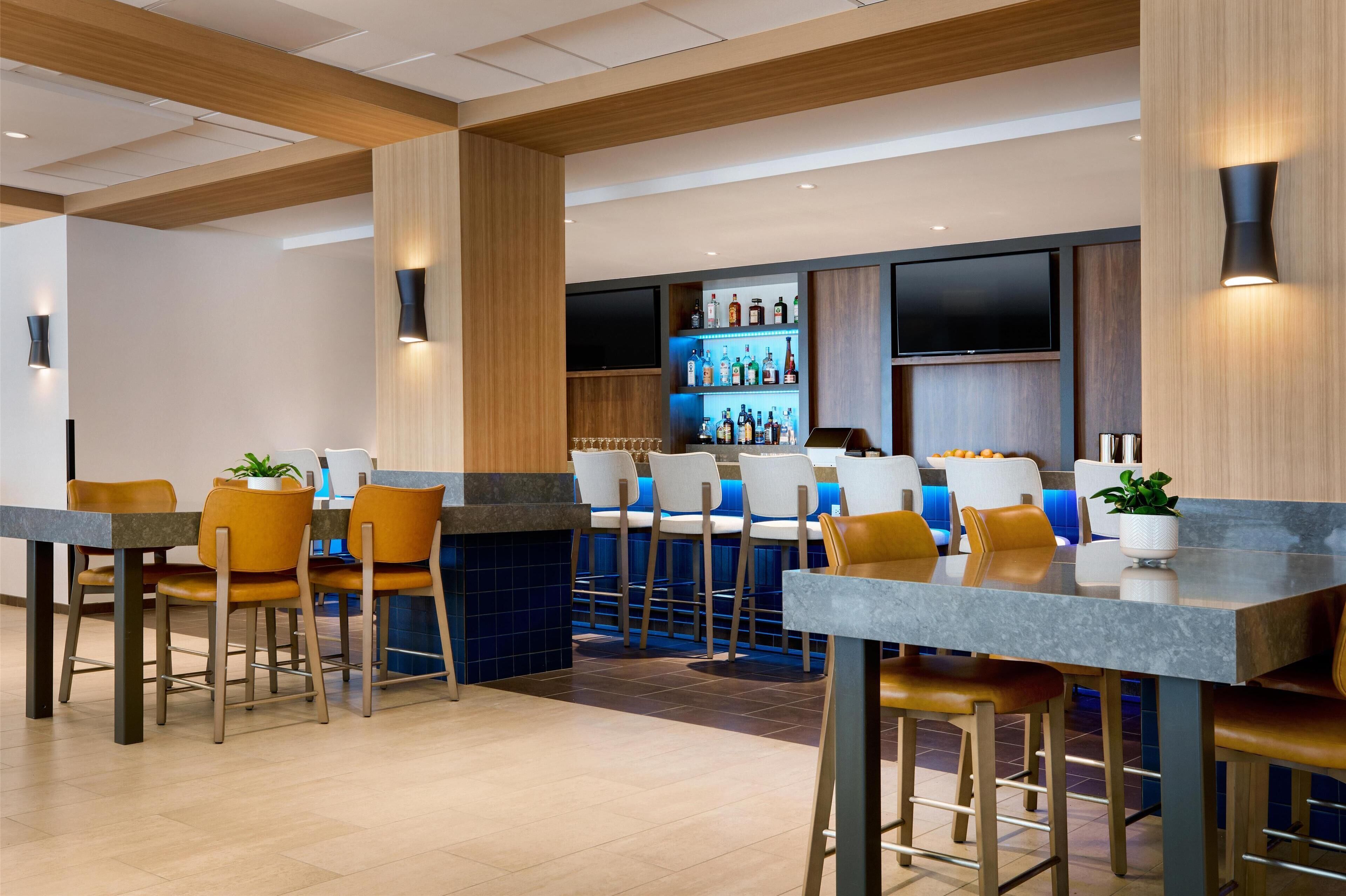 A modern bar area with bar stools, a counter, and a shelf of bottles.
