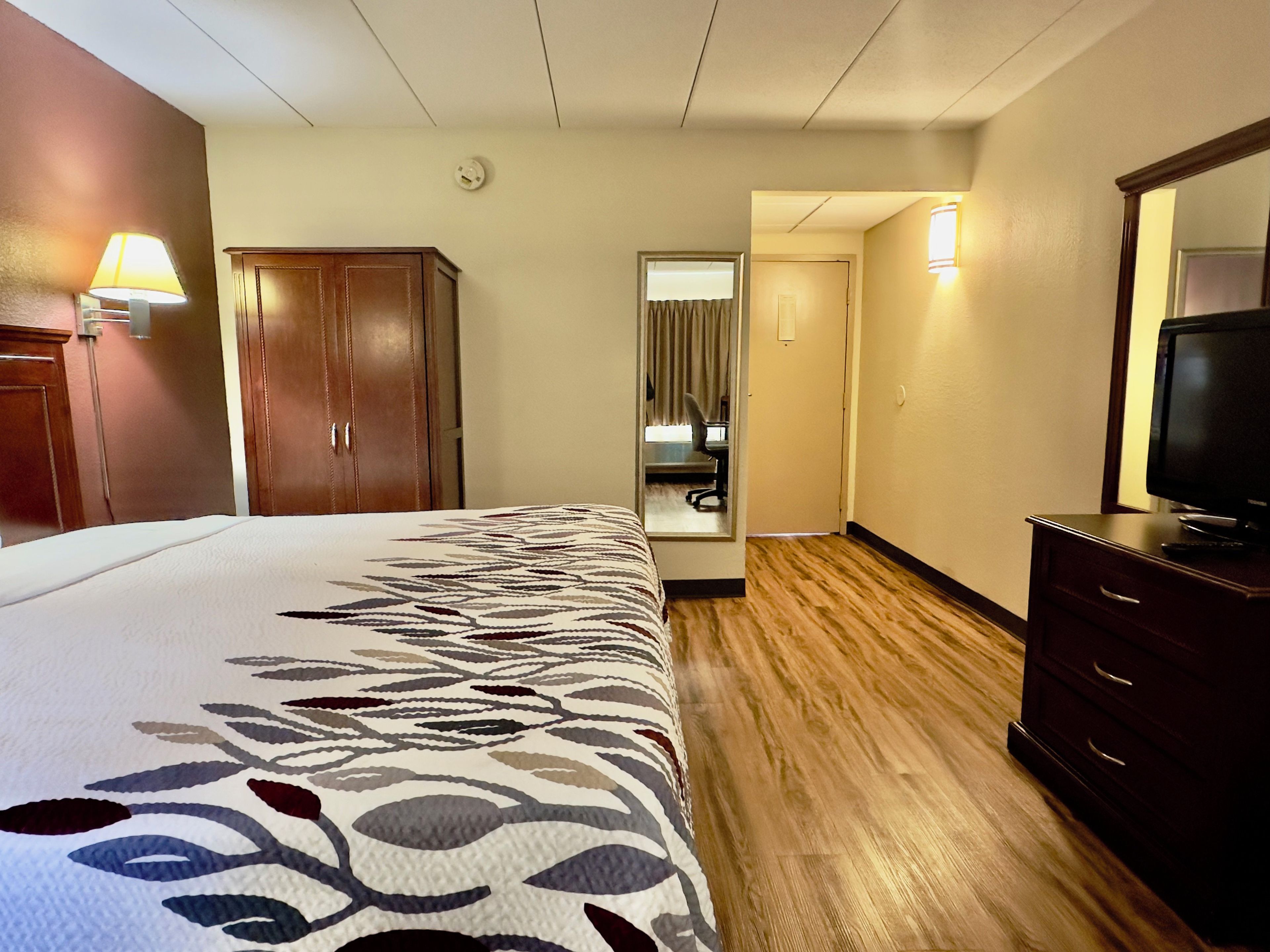 A hotel room with a bed, a desk, a chair, a television, and a wardrobe.