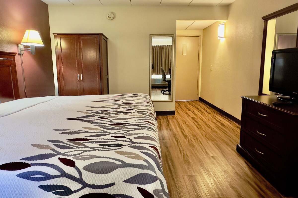 A hotel room with a bed, a desk, a chair, a television, and a wardrobe.