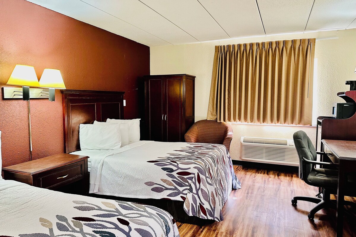 A hotel room with two beds, a desk, an air conditioner, and a chair.