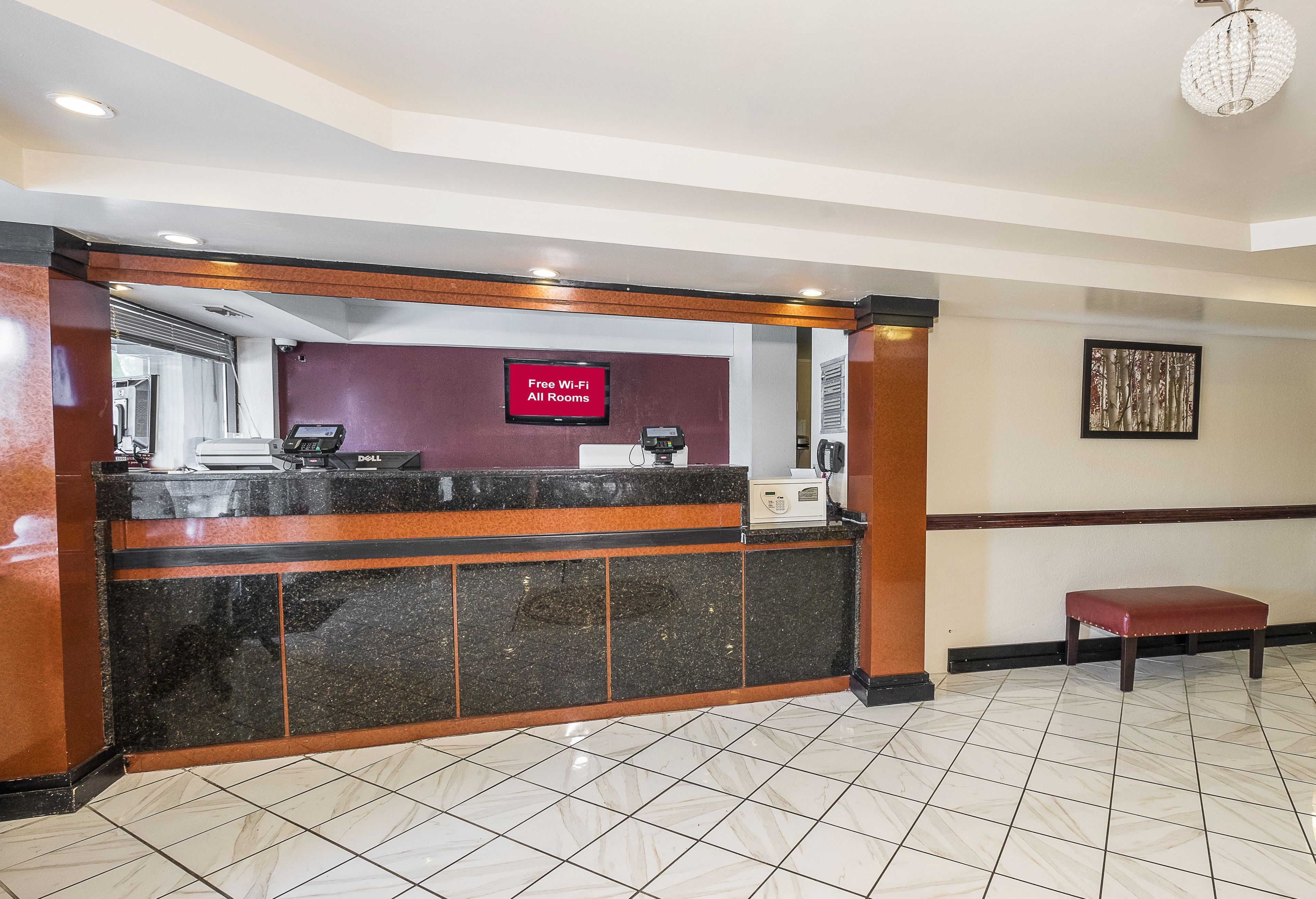 A hotel reception area with a marble floor, a reception desk, a 'Free Wi-Fi All Rooms' sign, a telephone, and a framed picture on the wall.