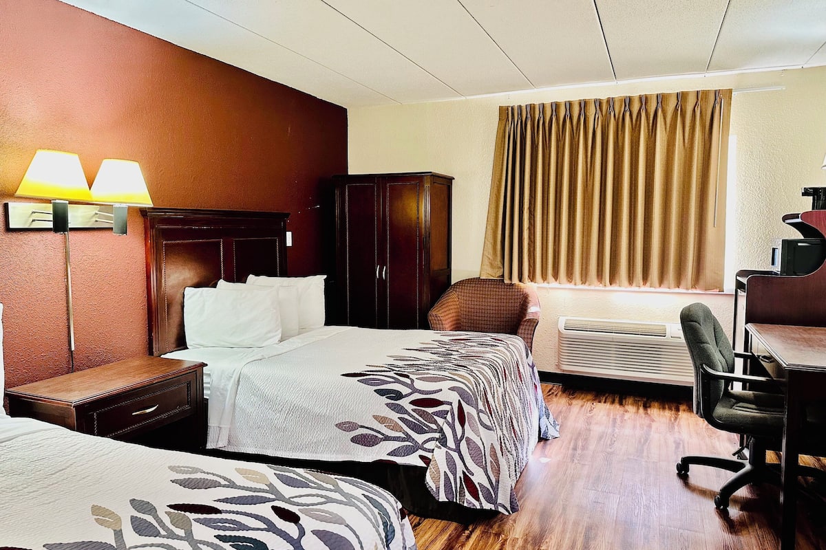 A hotel room with two beds, a desk, an air conditioner, and a chair.