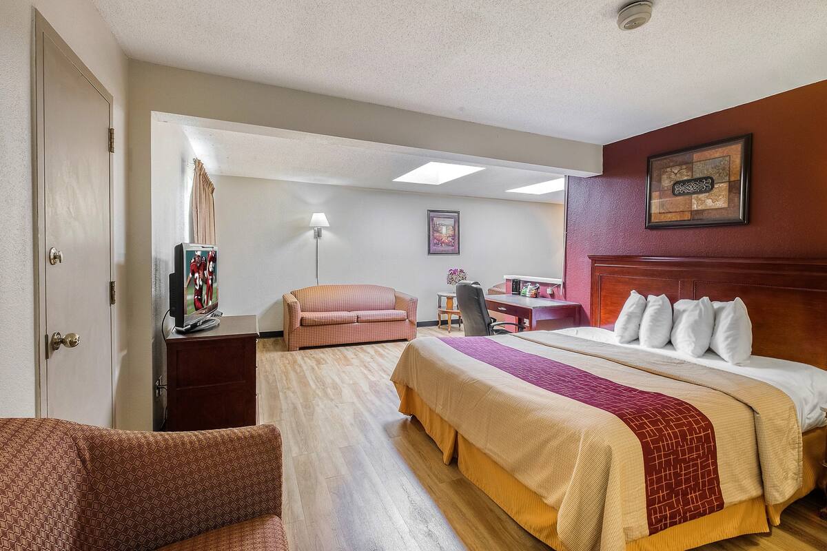 A hotel room with a large bed, a desk, a chair, a television, and a couch.