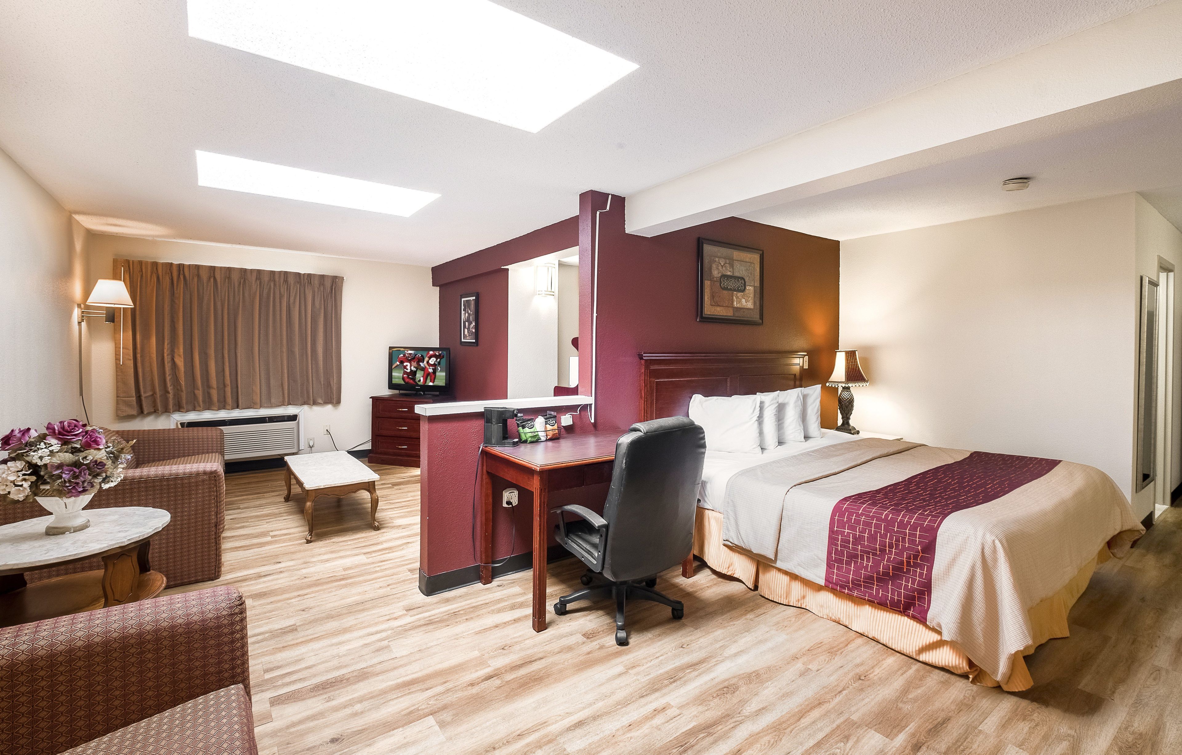 Une chambre d’hôtel avec un lit, un bureau, une chaise et une petite table sur laquelle est posé un vase de fleurs.