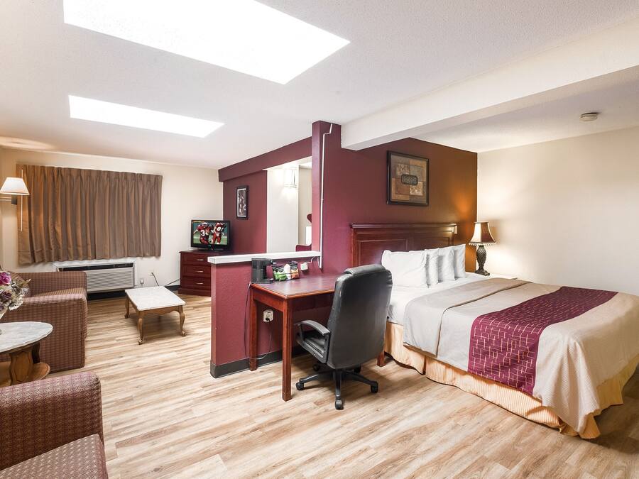 Quarto de hotel com cama, escrivaninha, cadeira e pequena mesa com um vaso de flores.