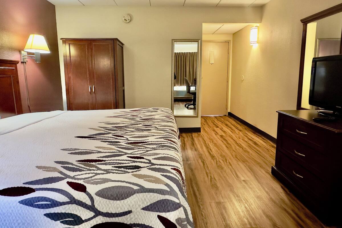 A hotel room with a bed, a desk, a chair, a television, and a wardrobe.
