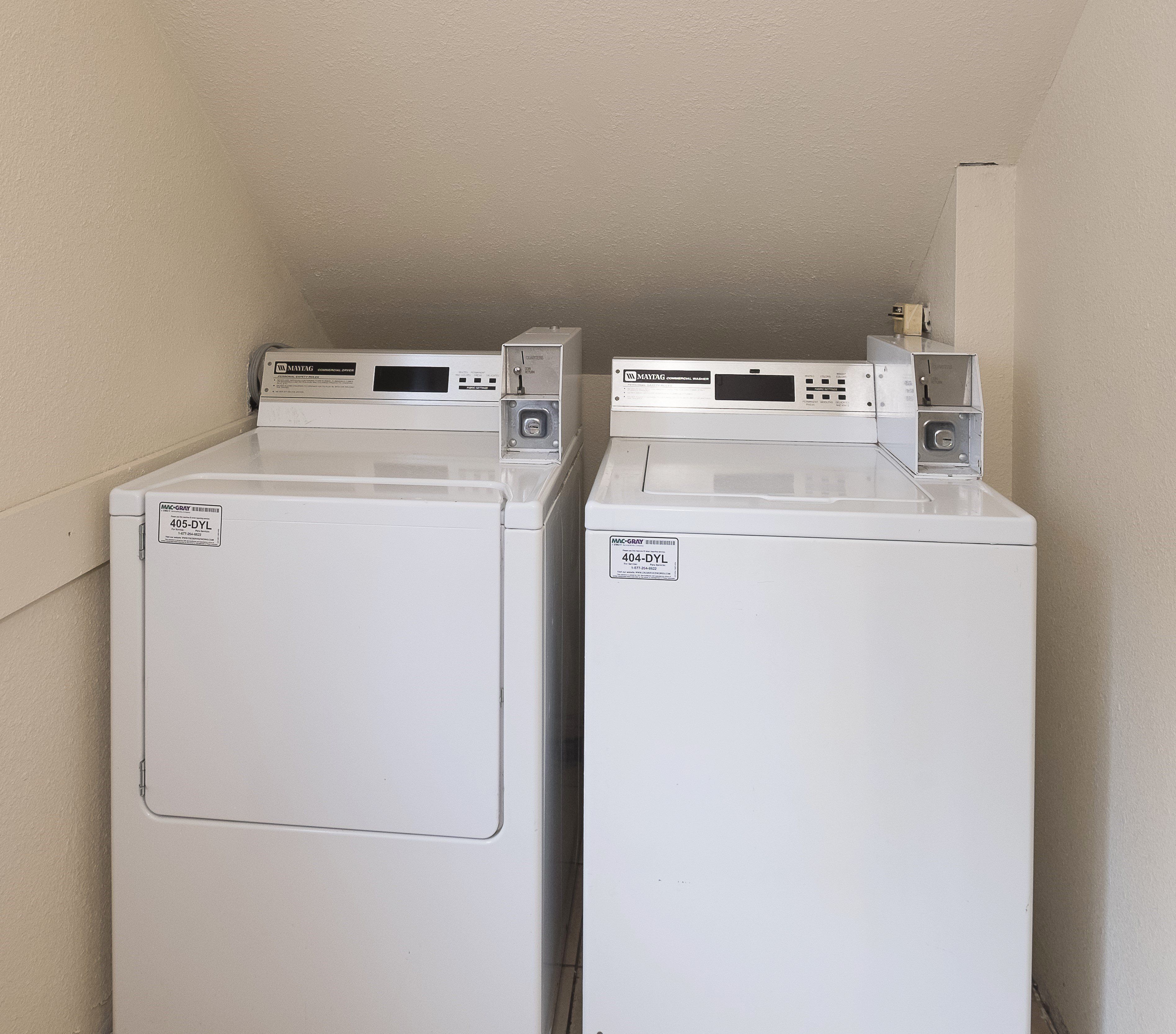 Deux machines à laver à chargement frontal, de couleur blanche, dotées de panneaux de commande, sont placées contre un mur uni.