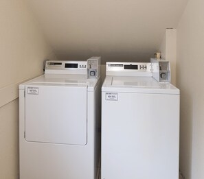 Two white front-loading washing machines with control panels, placed against a plain wall. - Red Roof Inn Hartford - Vernon (Vernon)