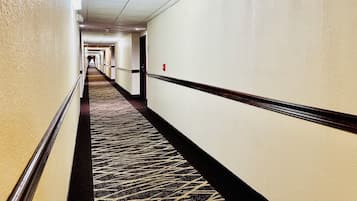 Un couloir d'hôtel avec des revêtements de sol en moquette, des murs blancs et des portes donnant accès aux chambres.