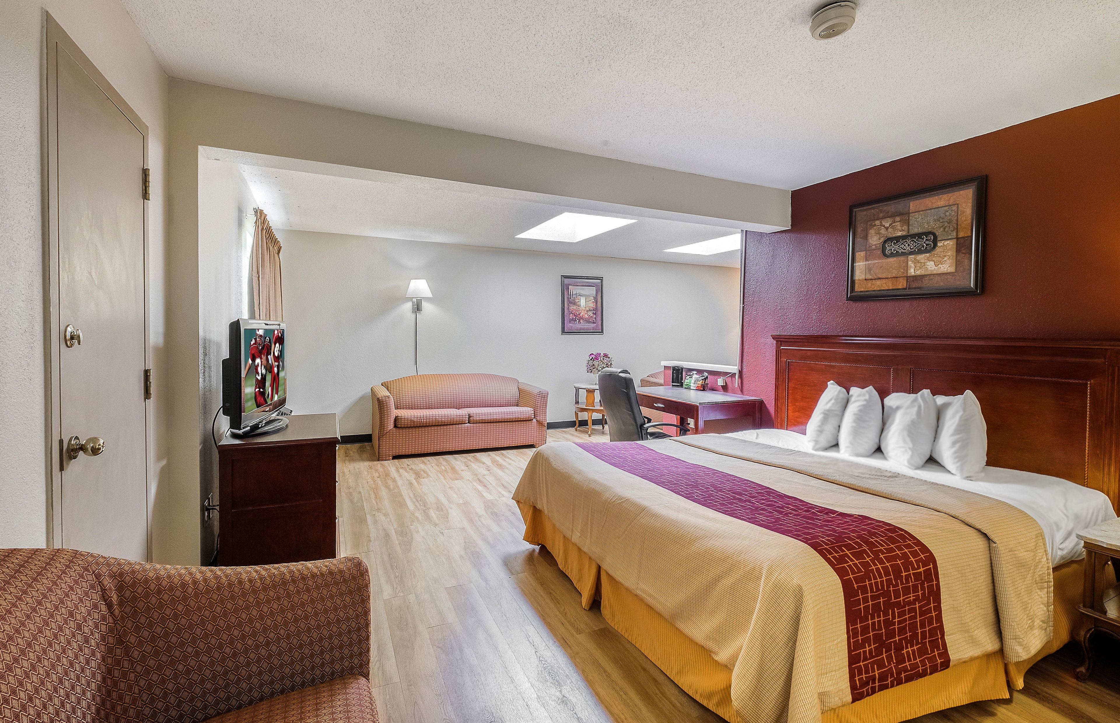 Habitación de hotel con una cama, un escritorio, una silla, un televisor y un cuadro en la pared.