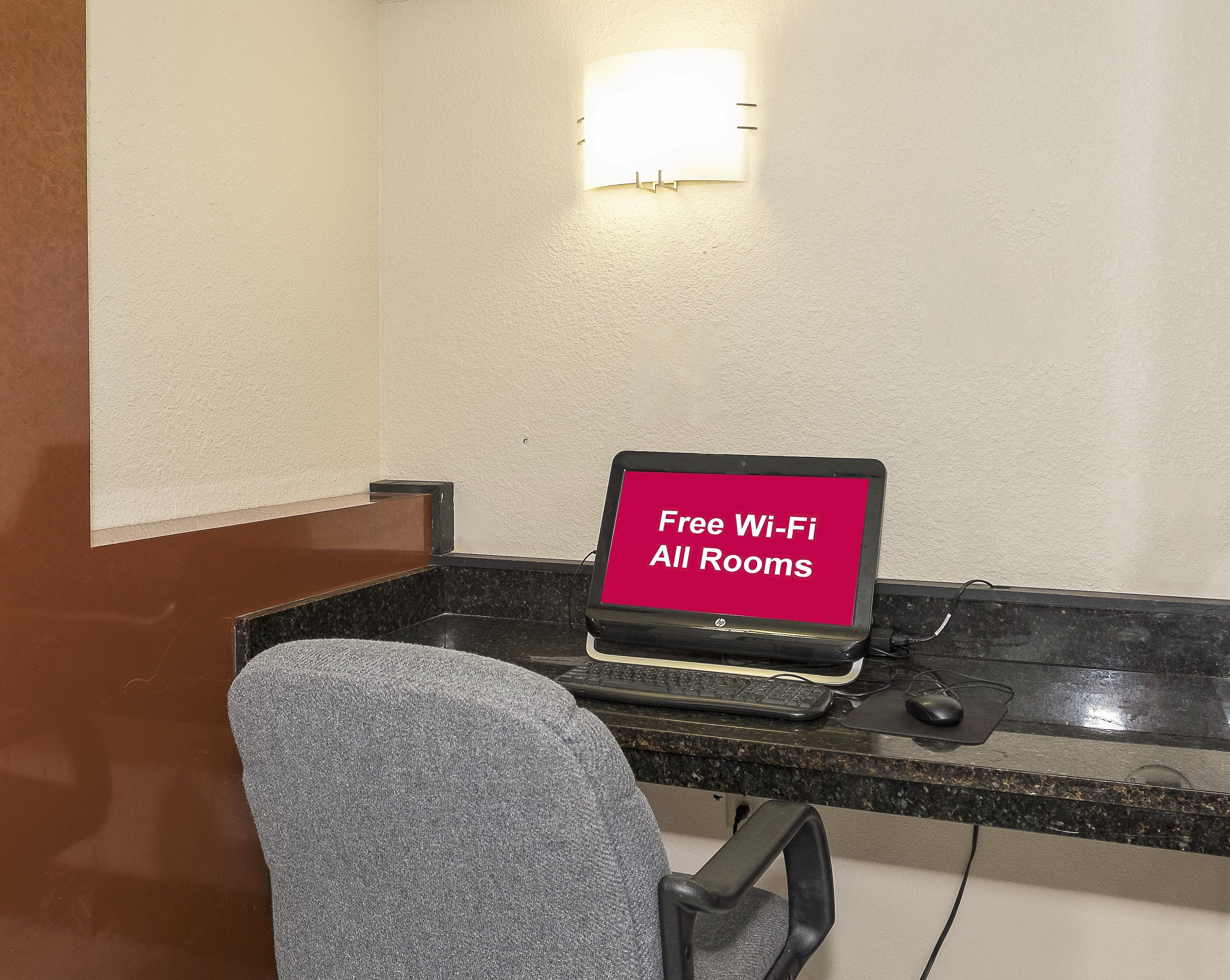 Un espacio de trabajo con una computadora portátil mostrando 'Free Wi-Fi All Rooms' y una silla.