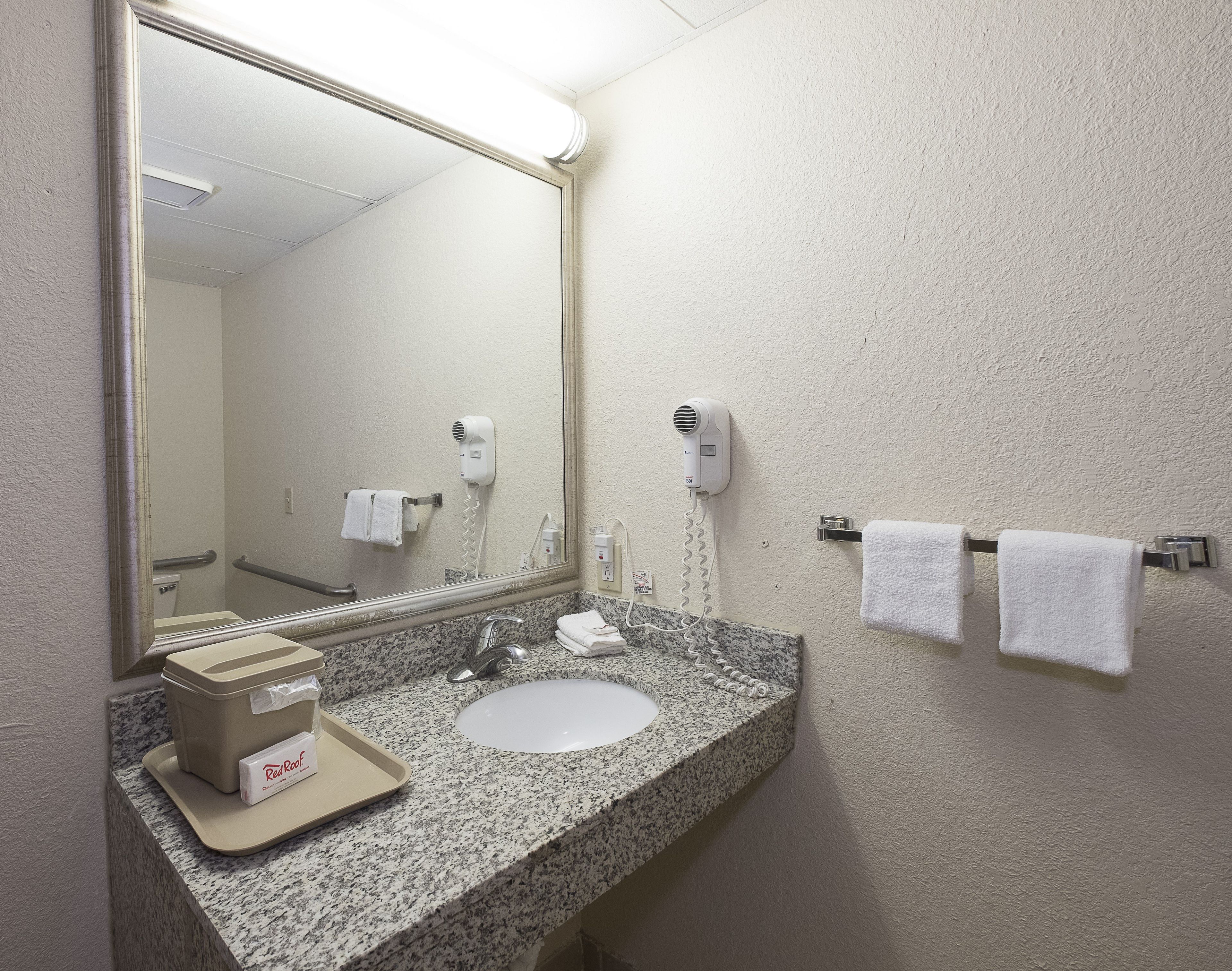 Une salle de bain avec un comptoir en granit, un lavabo blanc, un miroir, un sèche-cheveux et un porte-serviettes.