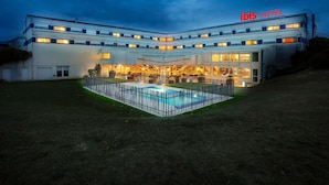 A hotel with a pool, multiple floors, and a sign reading 'ibis HOTEL'.