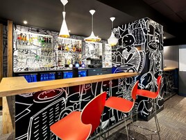 Zona de bar con diseño moderno, que incluye una barra con diferentes botellas y copas, y sillas rojas.