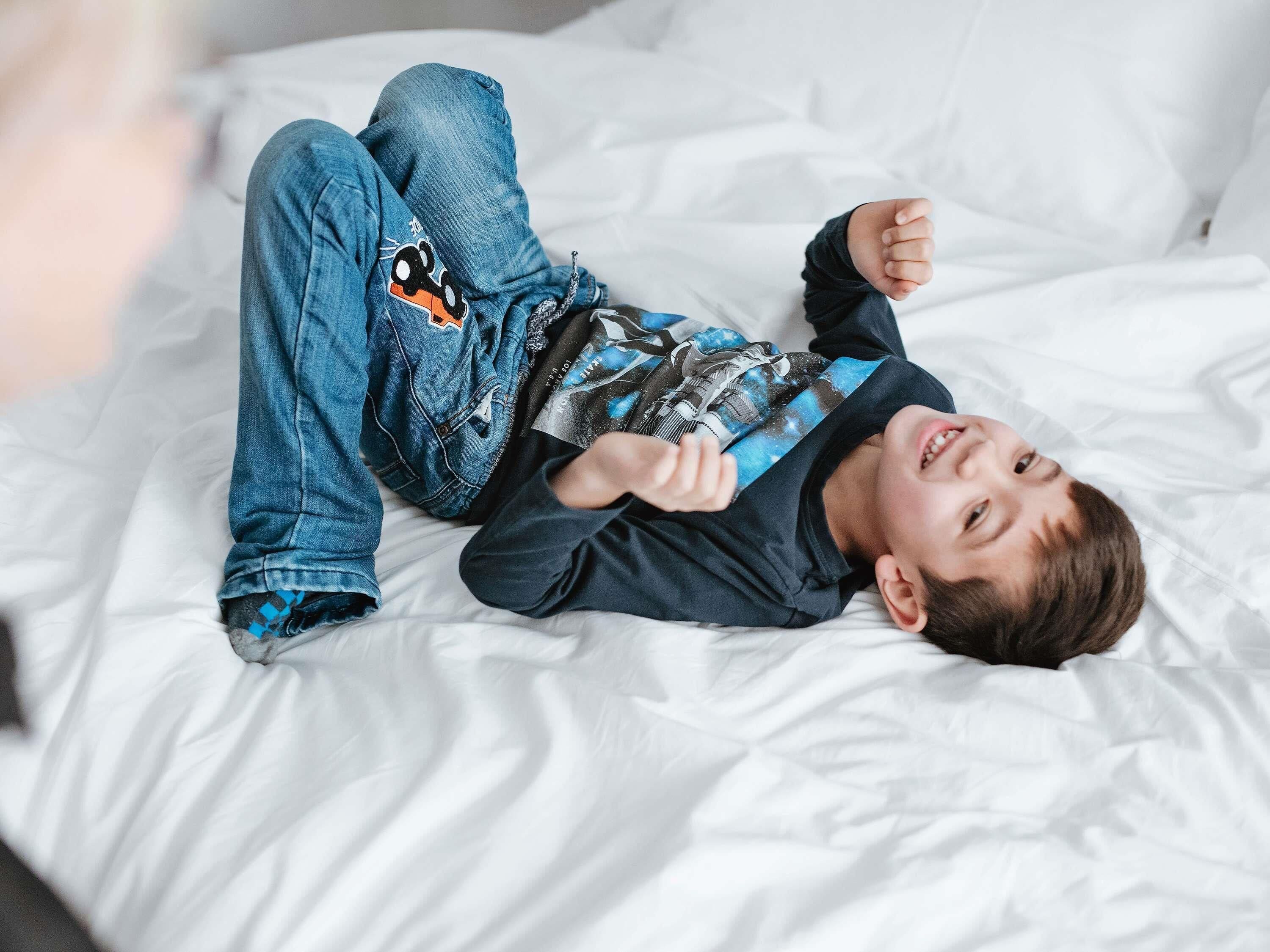 A person lying on a bed with white bedding.