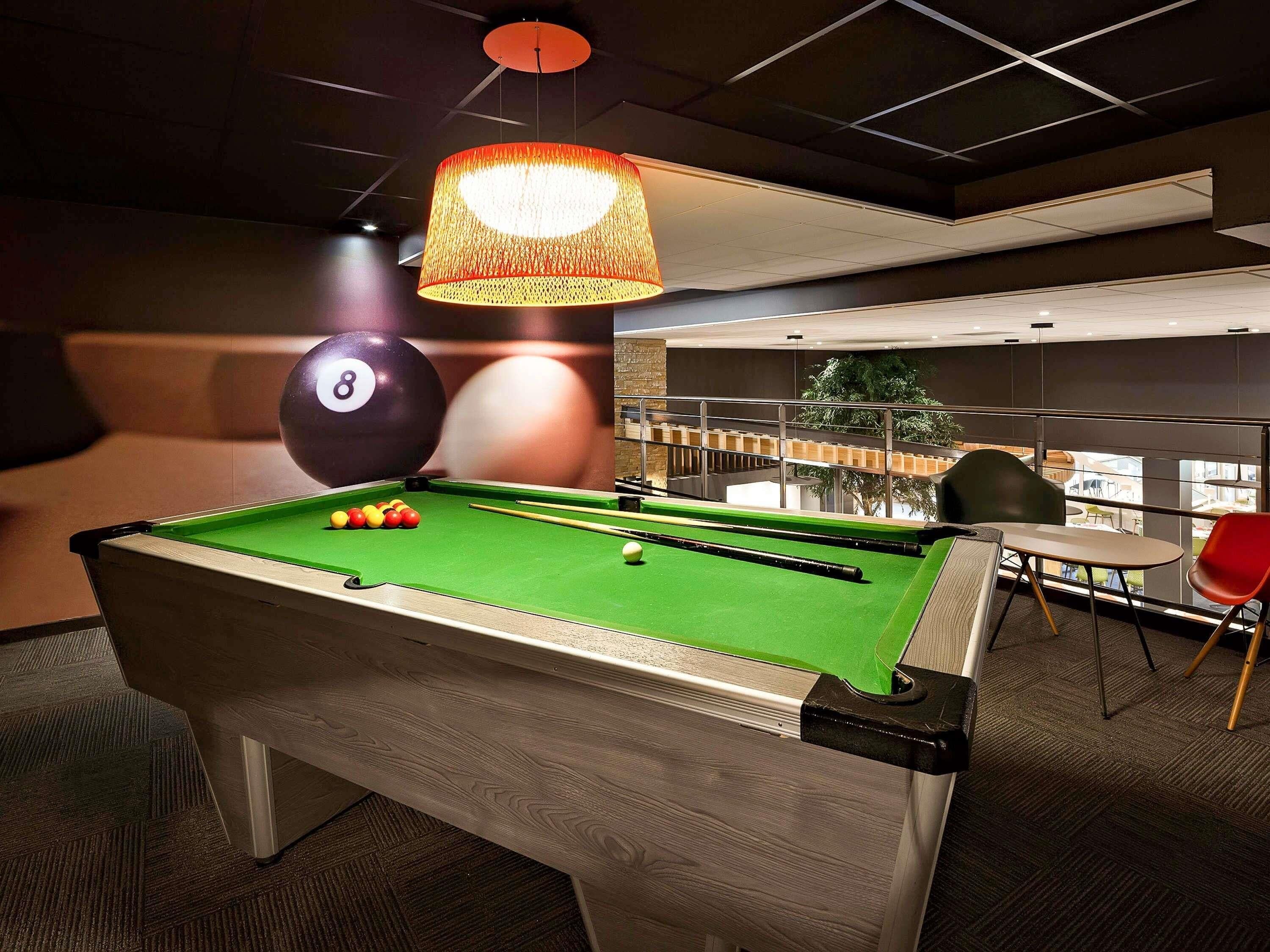 A pool table with balls, a billiard cue, and a hanging lamp in a room with a view of a balcony and outdoor area.