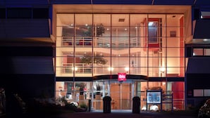 A modern hotel with a prominent "ibis HOTEL" sign, large glass windows, and a well-lit entrance.