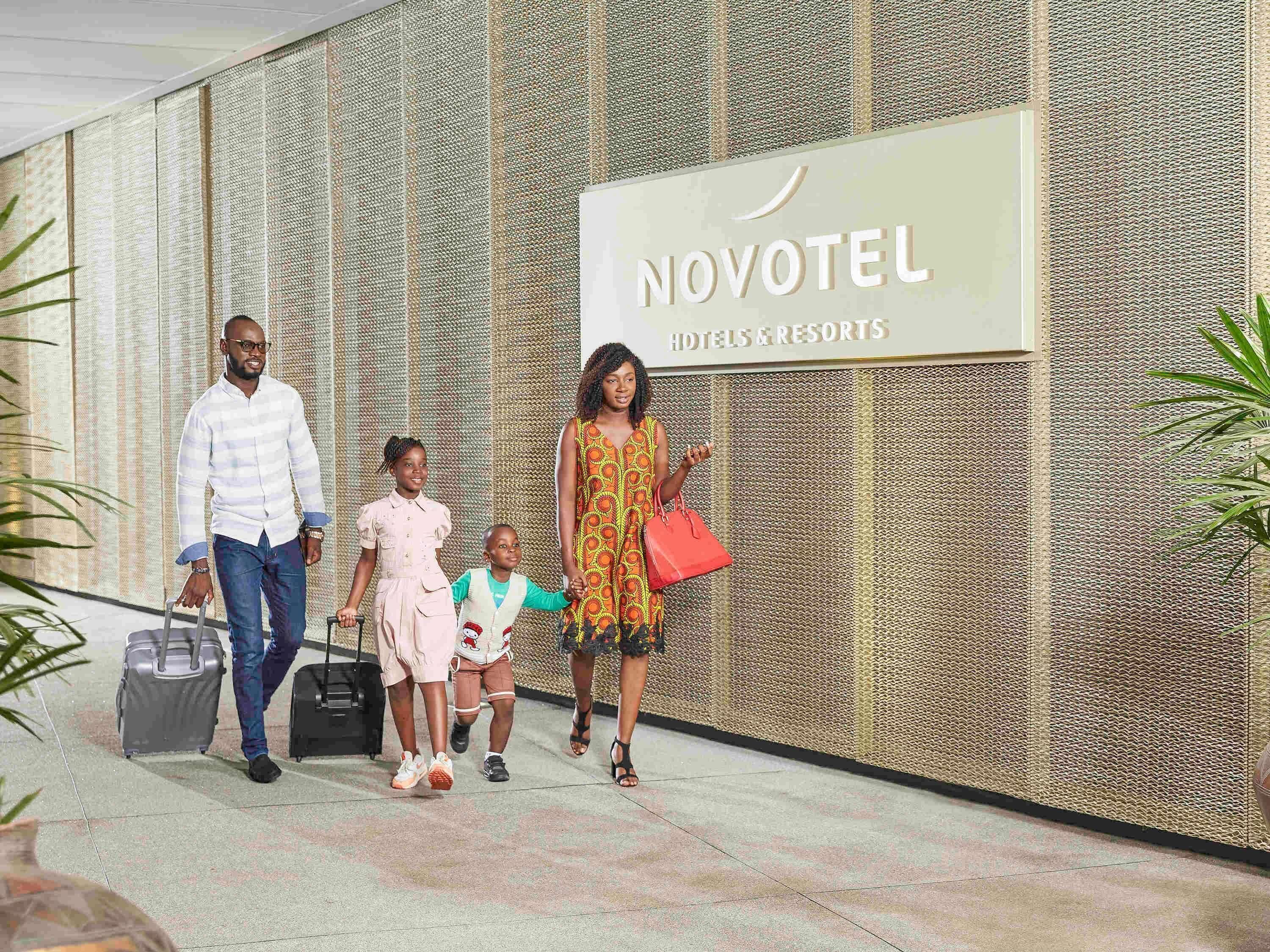 A family walking past a sign for Novotel Hotels & Resorts.