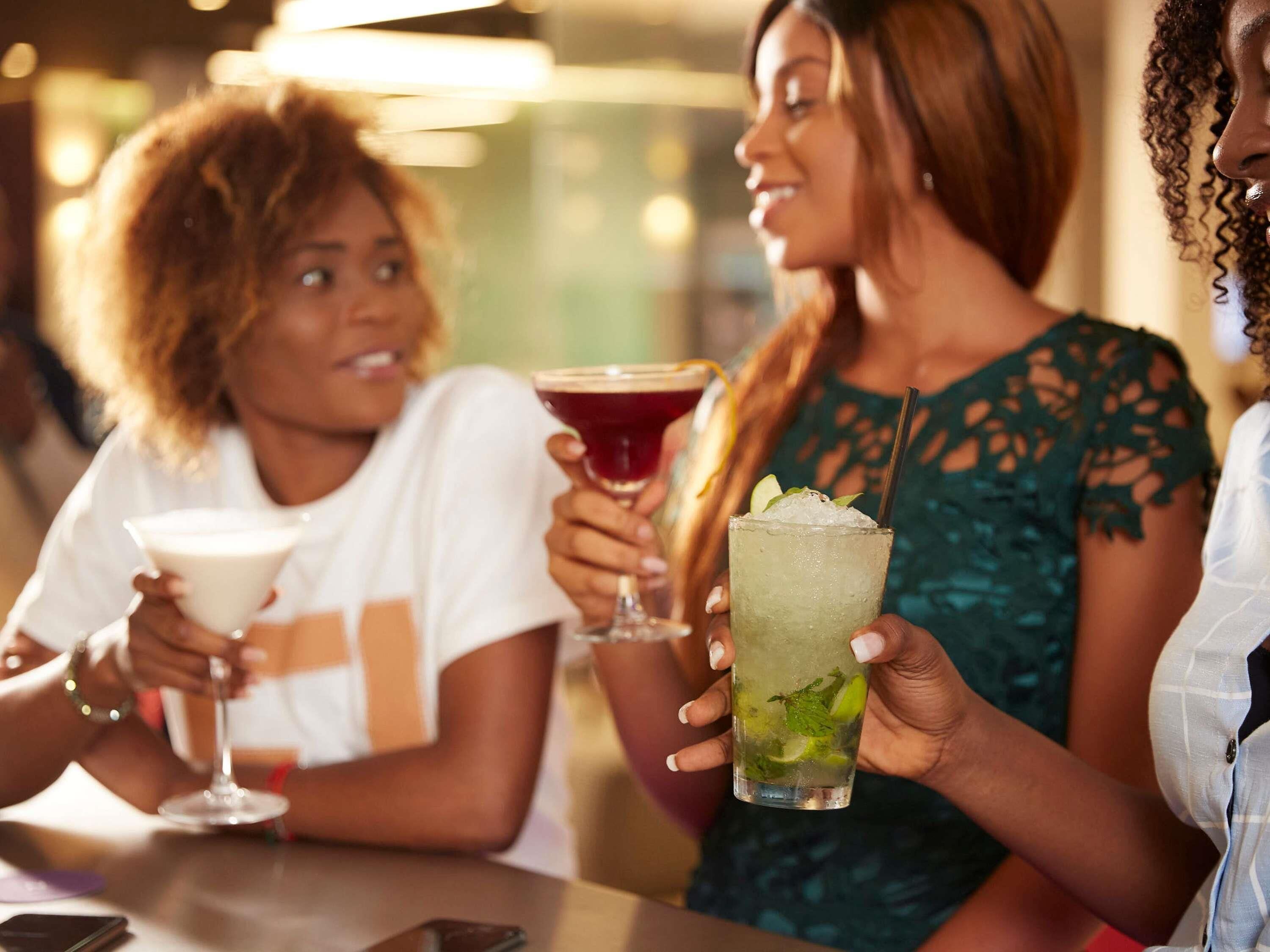 Drei Personen halten in einer Bar Getränke.