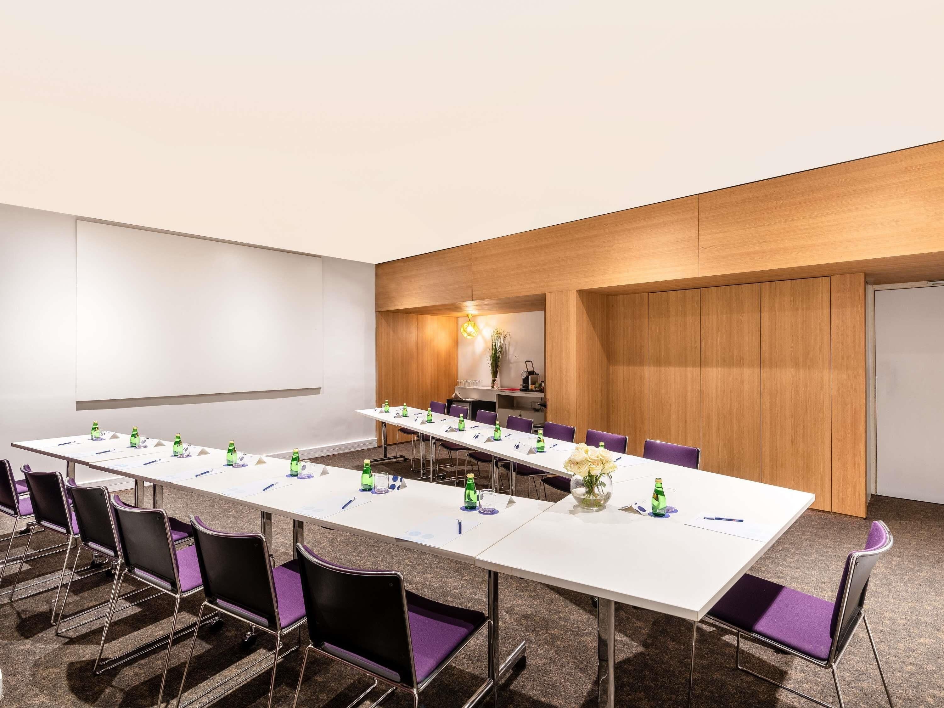 A conference room with a long table, purple chairs, and a projector screen.