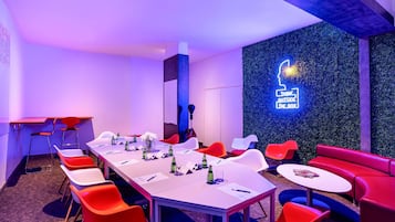 Une salle de conférence avec une longue table, des chaises rouges et blanches, et un panneau lumineux au néon sur le mur.