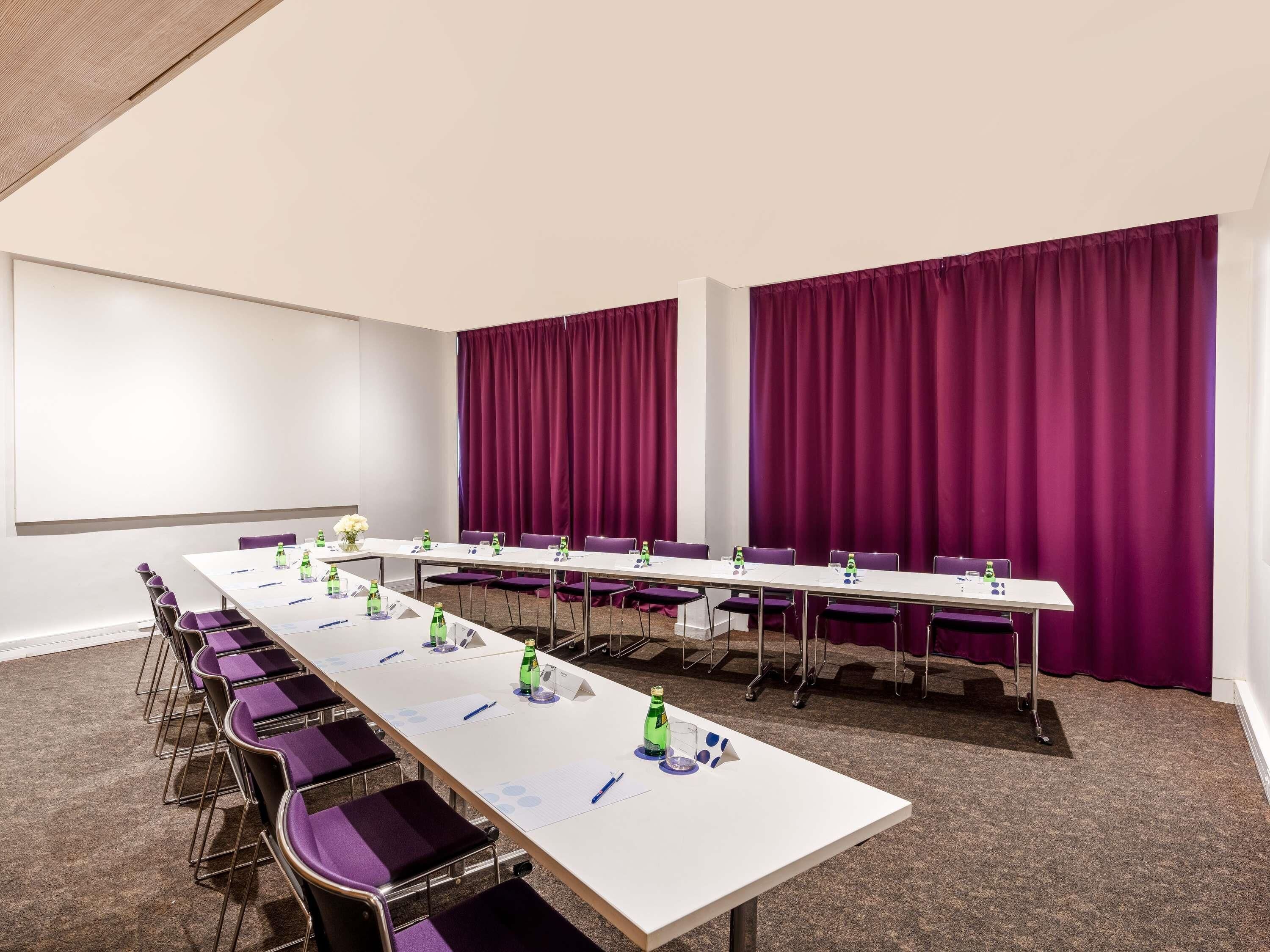 Ein Konferenzraum mit einem langen Tisch, violetten Stühlen, einer Projektionsleinwand und violetten Vorhängen.