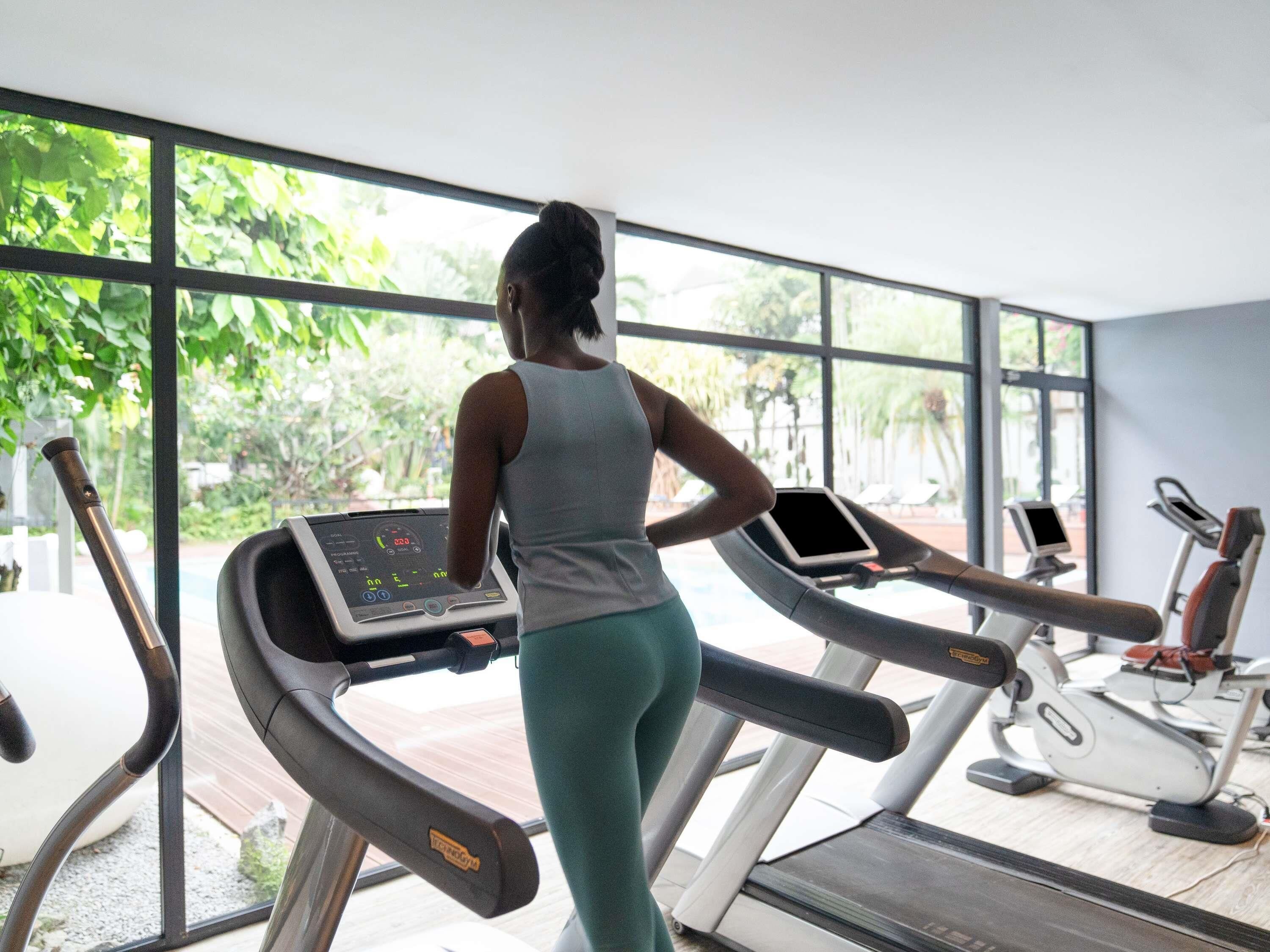 A woman using a treadmill in a gym with large windows and exercise equipment.