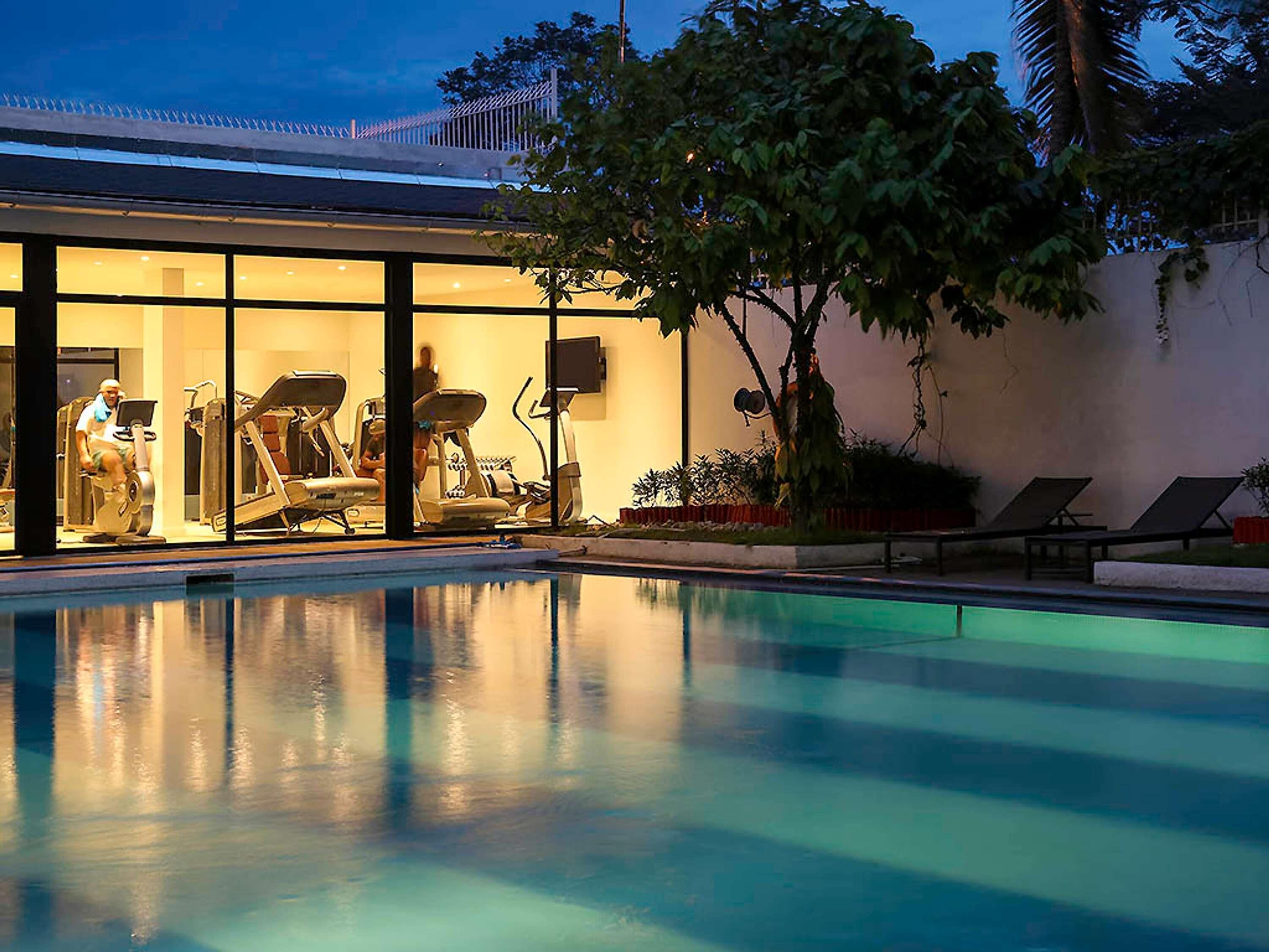A swimming pool with exercise equipment, a covered area with a view of the sky, and a tree.