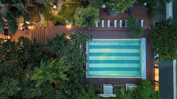 Vue aérienne d’une piscine sur le toit, entourée d’une végétation luxuriante et d’une terrasse en bois.