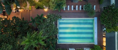 An aerial view of a rooftop pool surrounded by lush greenery and a wooden deck.