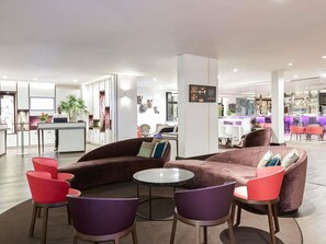Eine moderne Hotelhalle mit Rezeption, einer Sitzecke mit Sofas und Sesseln sowie einer Bar im Hintergrund.