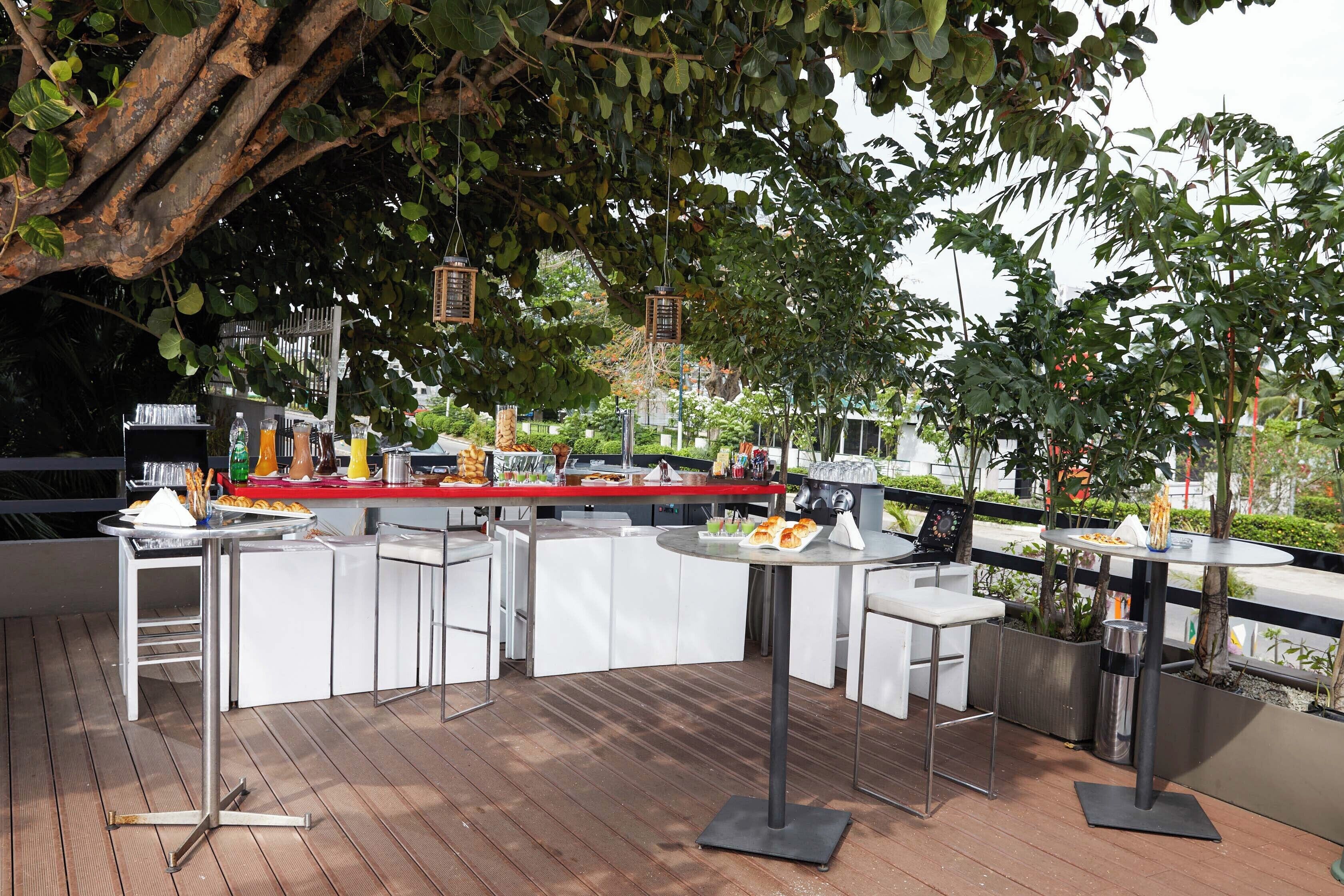 Zona de bar al aire libre con barra curva, taburetes blancos y vistas a la ciudad.