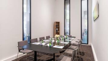 Un salón de conferencias con una larga mesa, sillas, botellas de agua y un reloj en la pared.