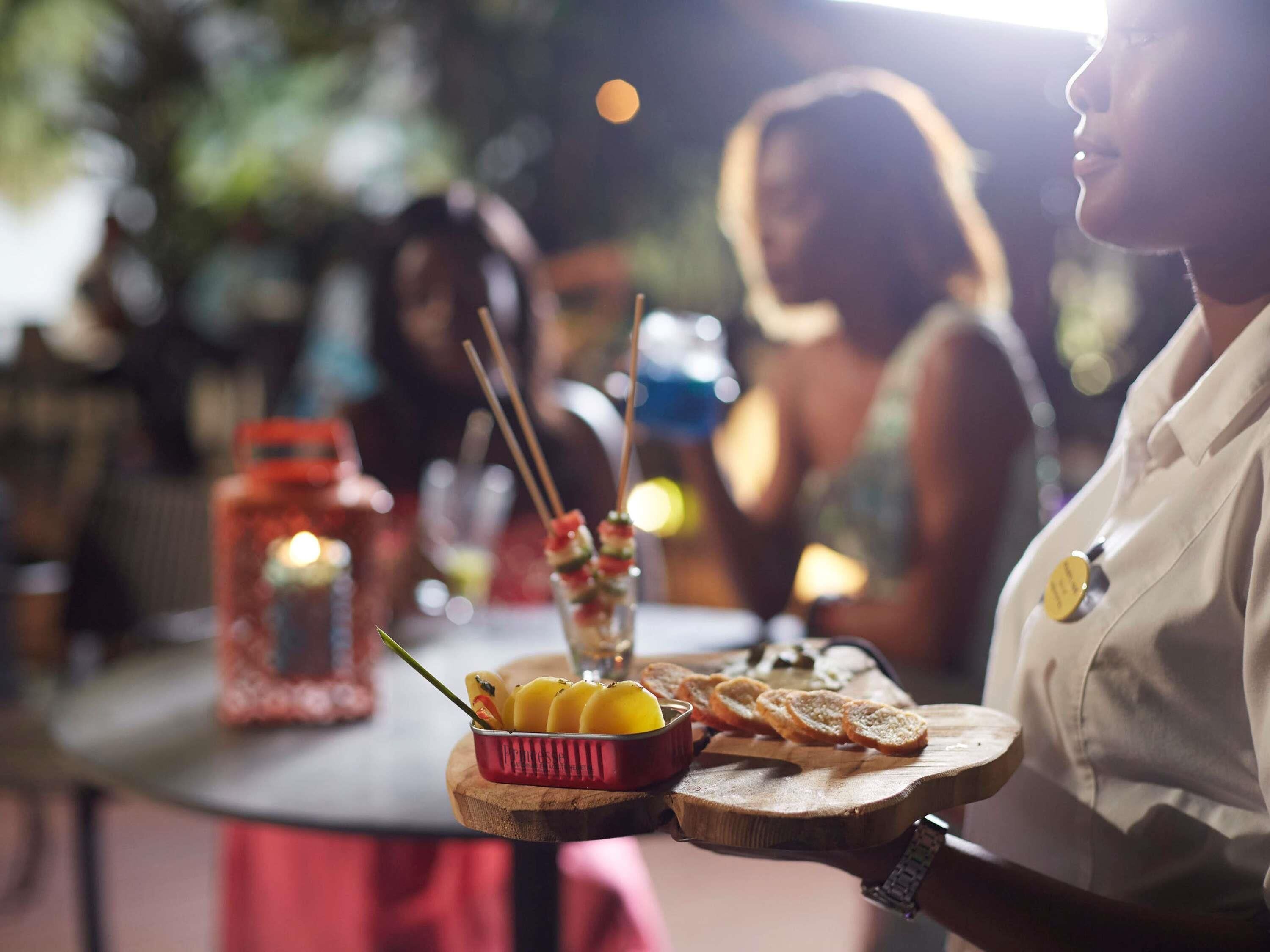 A person serving food on a wooden board with a basket of fruit and bread.