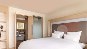 Habitación de hotel con una cama grande, cabecera de madera, baño con espejo y una mesita con un florero.