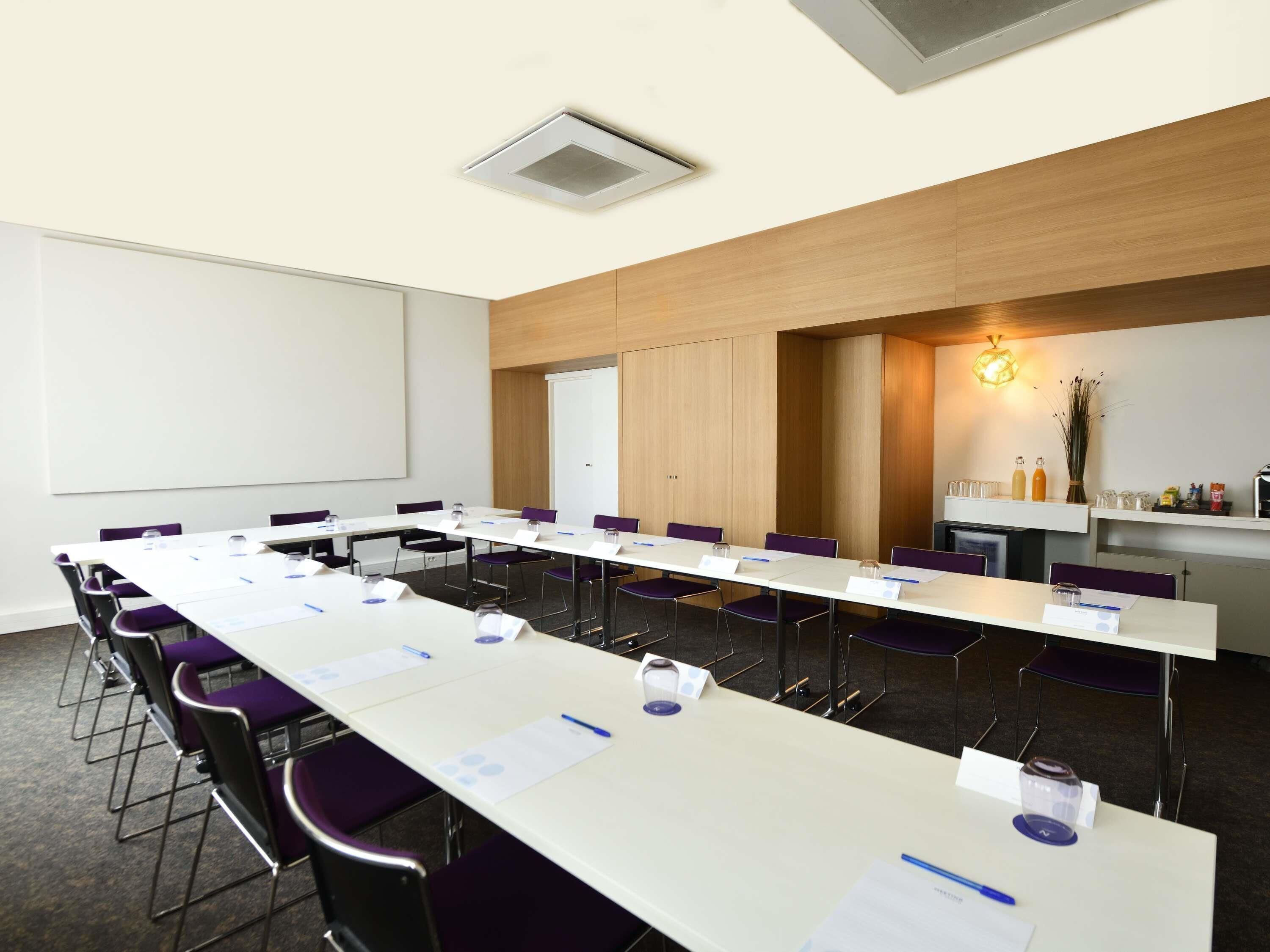 A conference room with a long table, chairs, a projector screen, and a whiteboard.