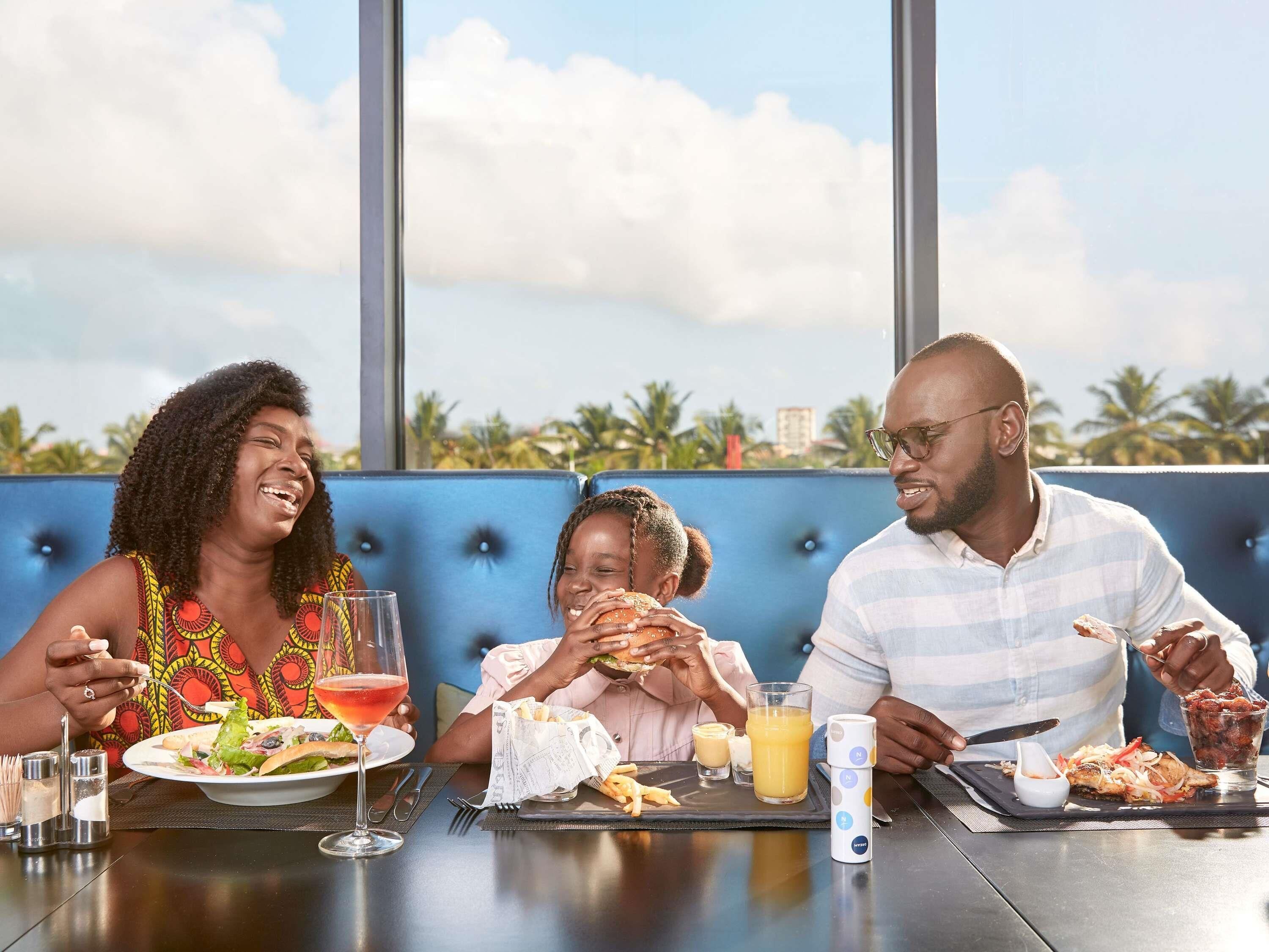 Three people dining at a table with a view of palm trees and a building in the background.