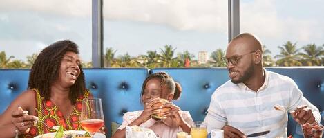 Three people dining at a table with a view of palm trees and a building in the background.