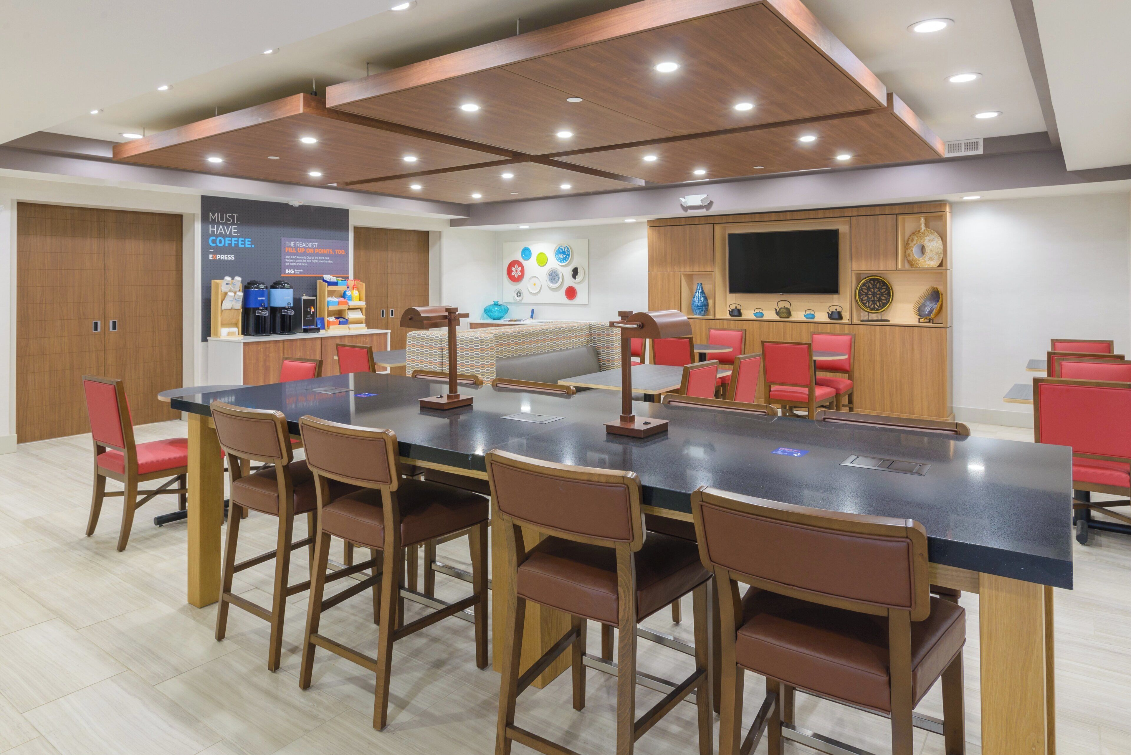 A modern meeting room with a long table, multiple chairs, a coffee station, and a television on the wall.
