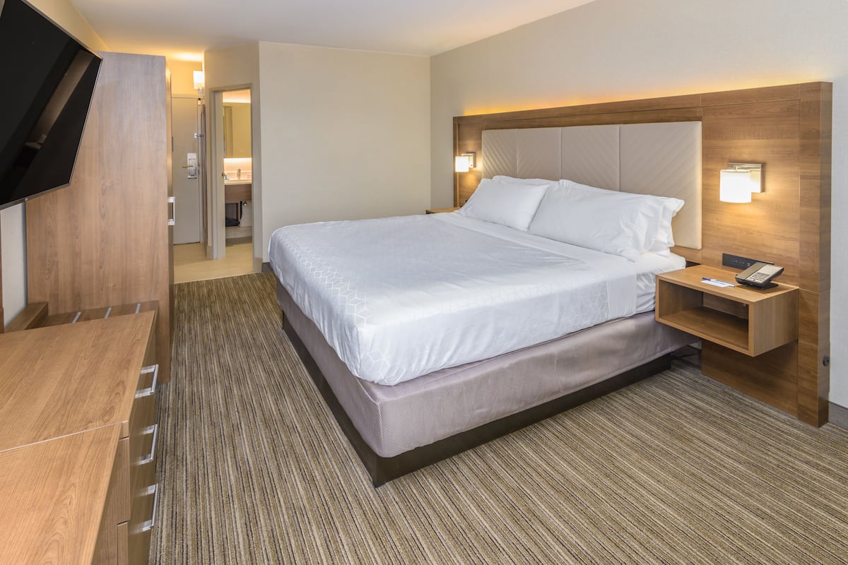 A hotel room with a large bed, a wooden nightstand, a TV, and a bathroom visible through an open door.