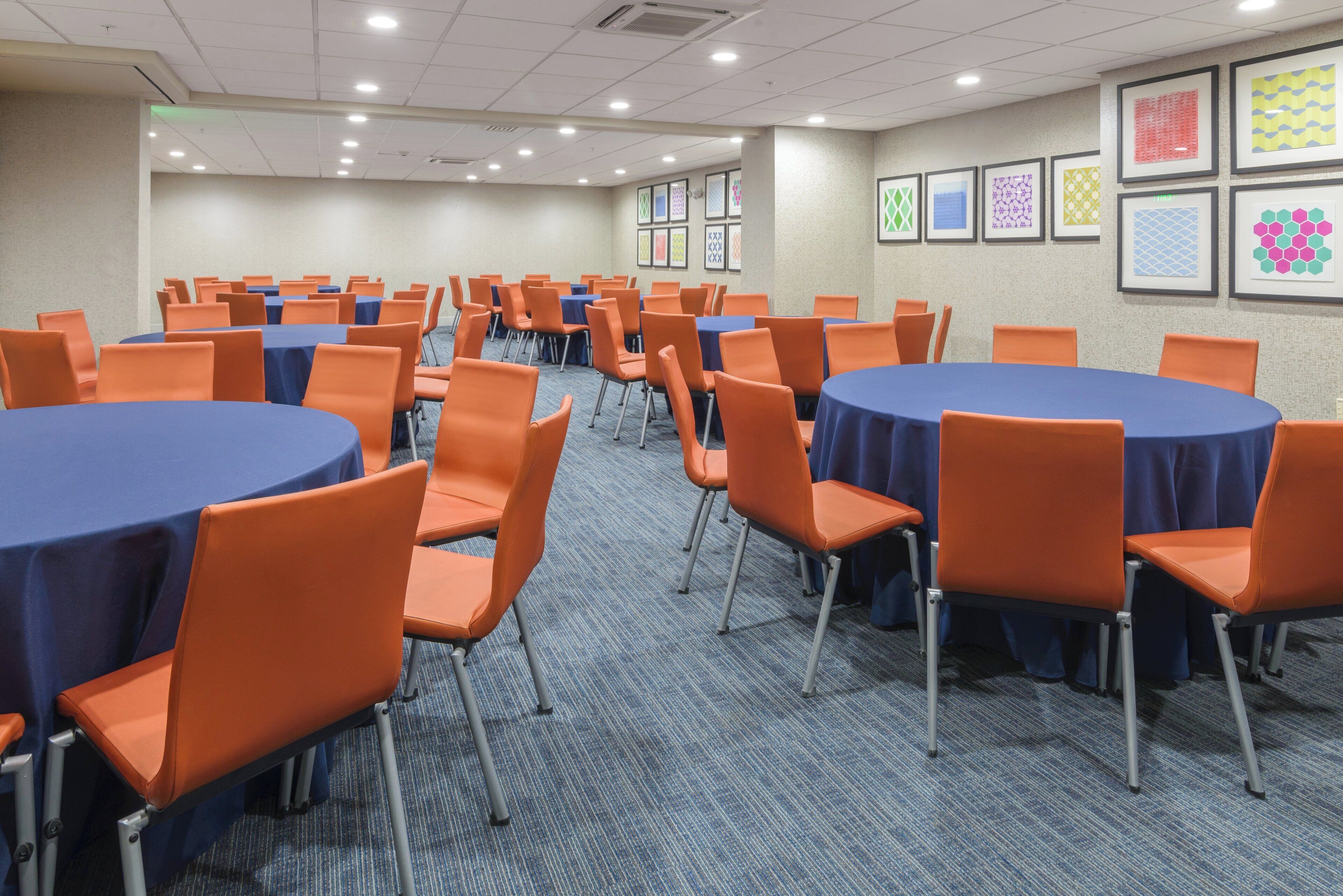 Une salle de conférence avec plusieurs tables rondes, des chaises orange et des nappes bleues.