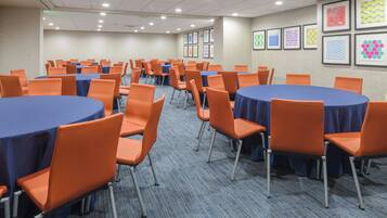 A conference room with multiple round tables, orange chairs, and blue tablecloths.