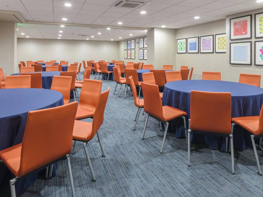 A conference room with multiple round tables, orange chairs, and blue tablecloths.