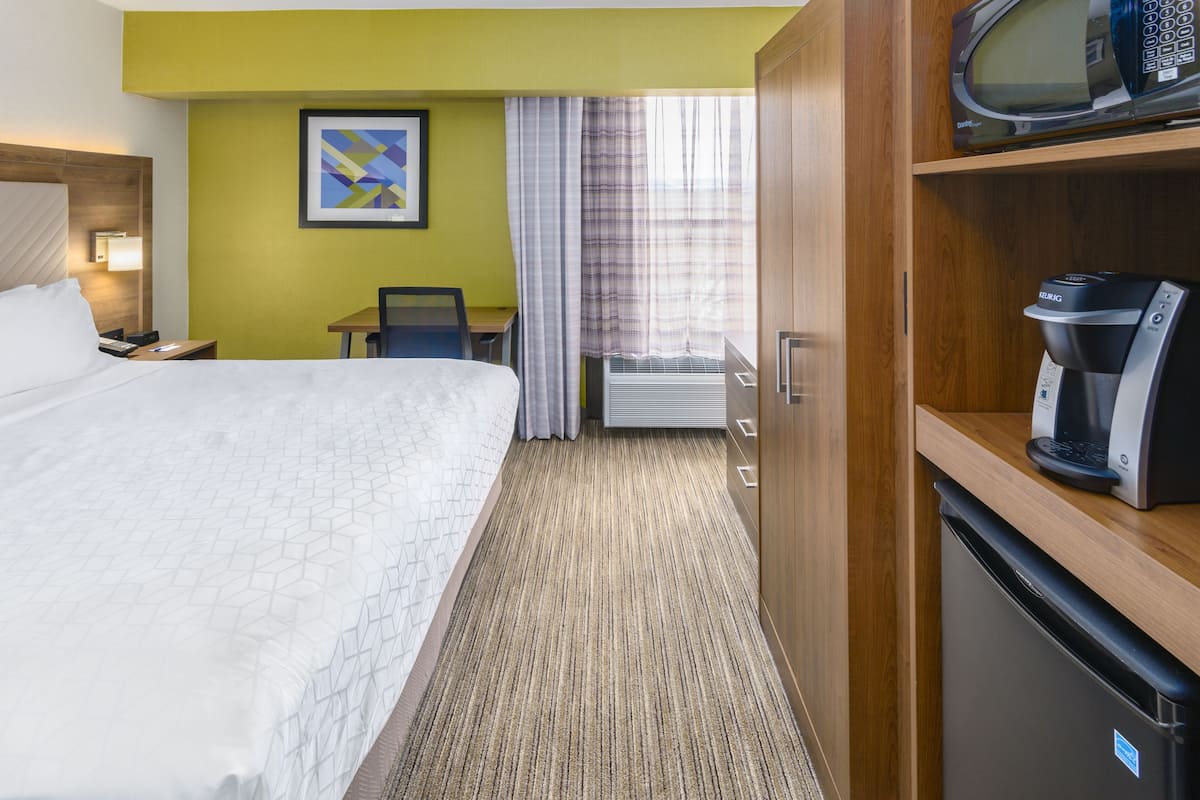 A hotel room with a bed, a desk, a microwave, and a coffee machine.
