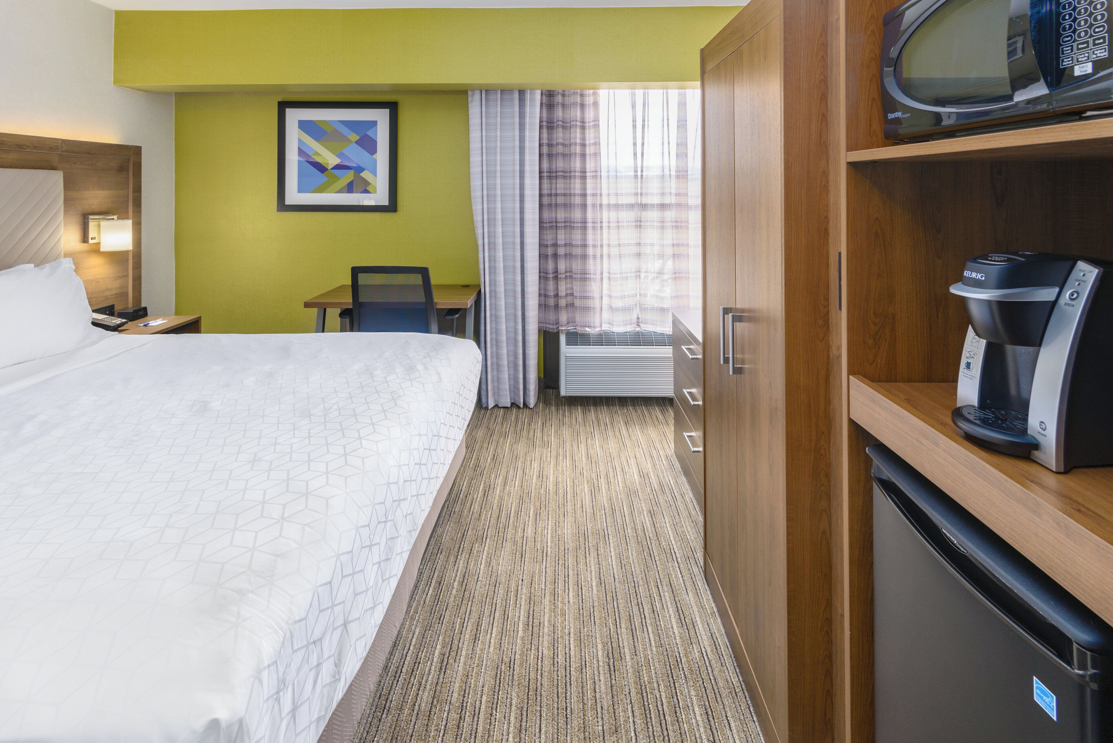 Une chambre d’hôtel équipée d’un lit, d’un bureau, d’une chaise, d’un four à micro-ondes et d’une machine à café.