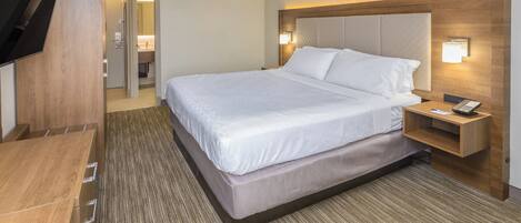 Una habitación de hotel con una cama grande, una mesita de noche con un teléfono y un televisor montado en la pared.